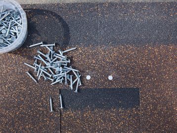 Scattered screws on a textured surface with two white objects.