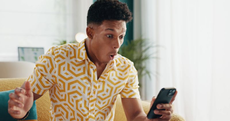 Man, excited and phone in home for win, gambling app and online game in living room. Winner, surprise and notification on mobile for announcement, reward program and bonus achievement on lottery