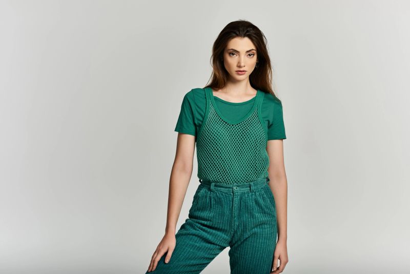 A beautiful young woman wears a trendy green outfit, striking a pose with poise and style.