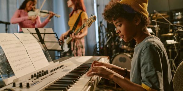 Young musicians rehearsing with keyboard, violin, and guitar in a studio.
