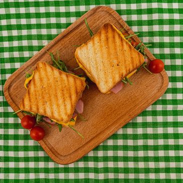 Two grilled sandwiches with cheese, ham, and greens on a wooden board.