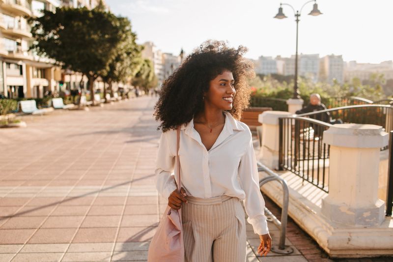 A young African woman walking through Malta's streets with a tote bag on her back. Simple and stylish.