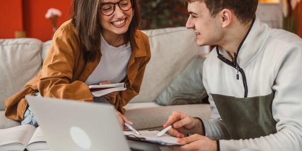 Two students happily studying together with laptop and books.