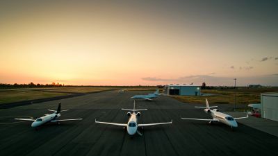 Three small jets parked on an airport runway at sunset.