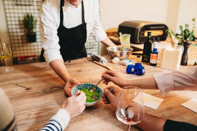 Chef presenting a vibrant pesto sauce to cooking class students, engaging them in a flavorful tasting experience filled with culinary learning