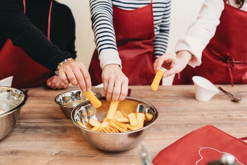 Three pastry chefs working together, grabbing biscuits from a metal bowl as they prepare a delicious tiramisu recipe in the kitchen