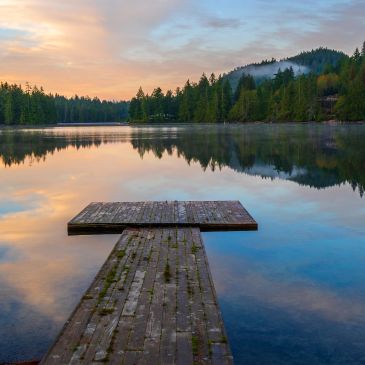 Serene lake with wooden dock at sunset.