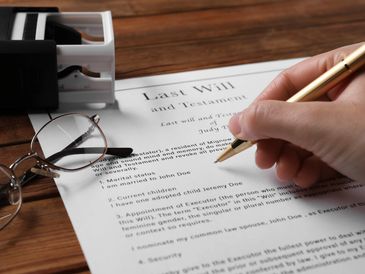 Someone holding a pen signing a document that reads: "Last Will and Testament"