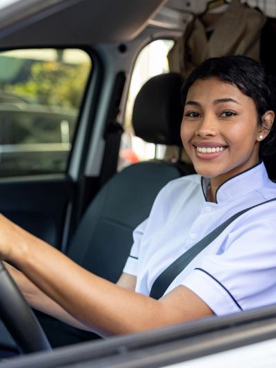 Smiling woman in a white uniform driving a car.