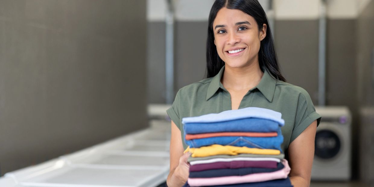 Woman holding folded laundry and smiling in a laundromat.