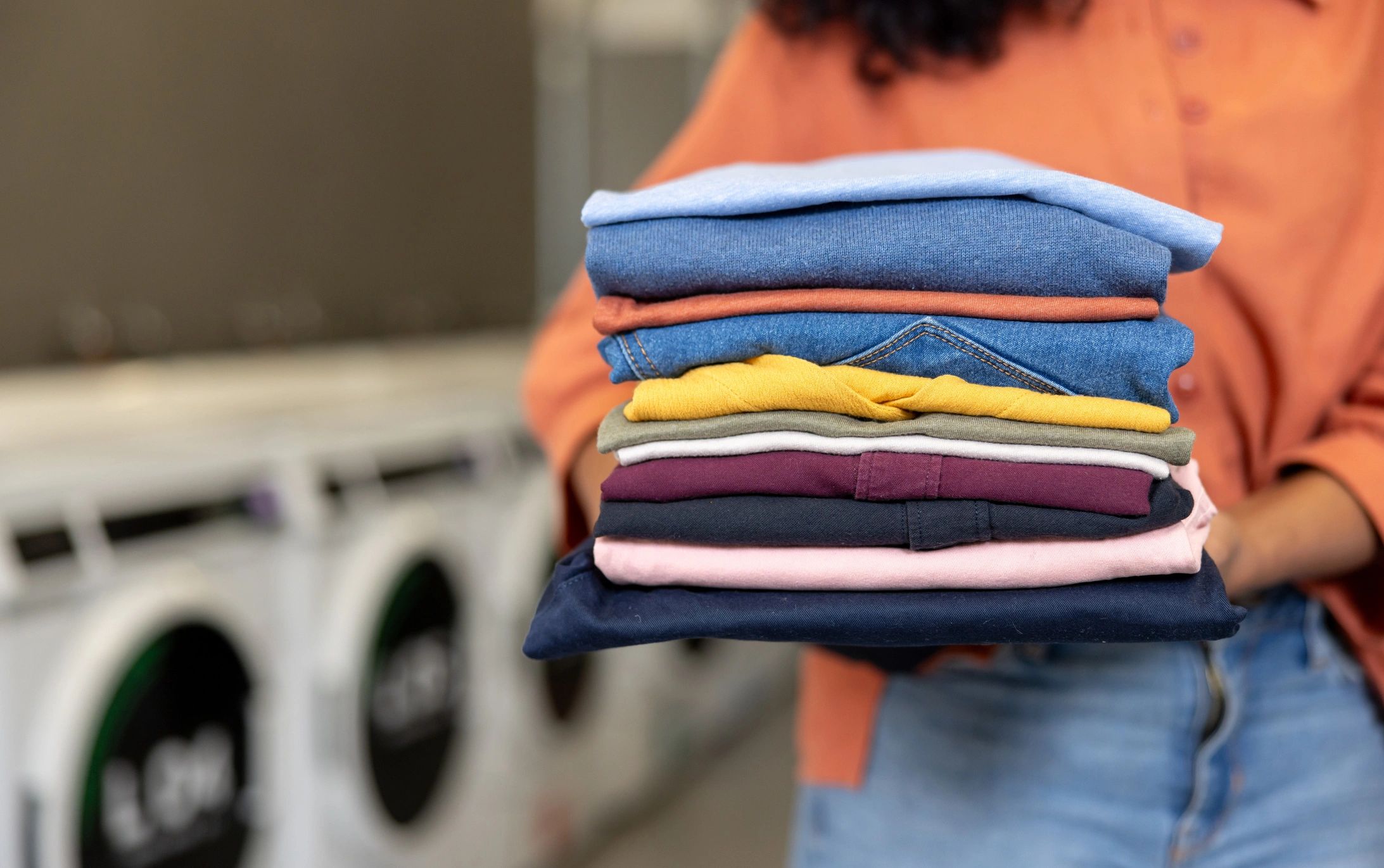 Person holding a neatly folded stack of colorful clothes in a laundry setting.
