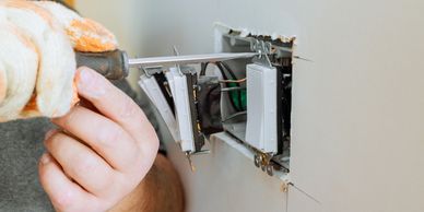 A person repairs electrical switches with a screwdriver on a wall.