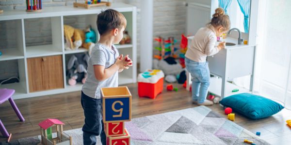 Two toddlers playing with blocks and toys in a bright playroom.