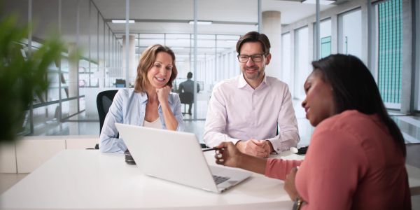 Three colleagues discussing work around a laptop in a modern office.