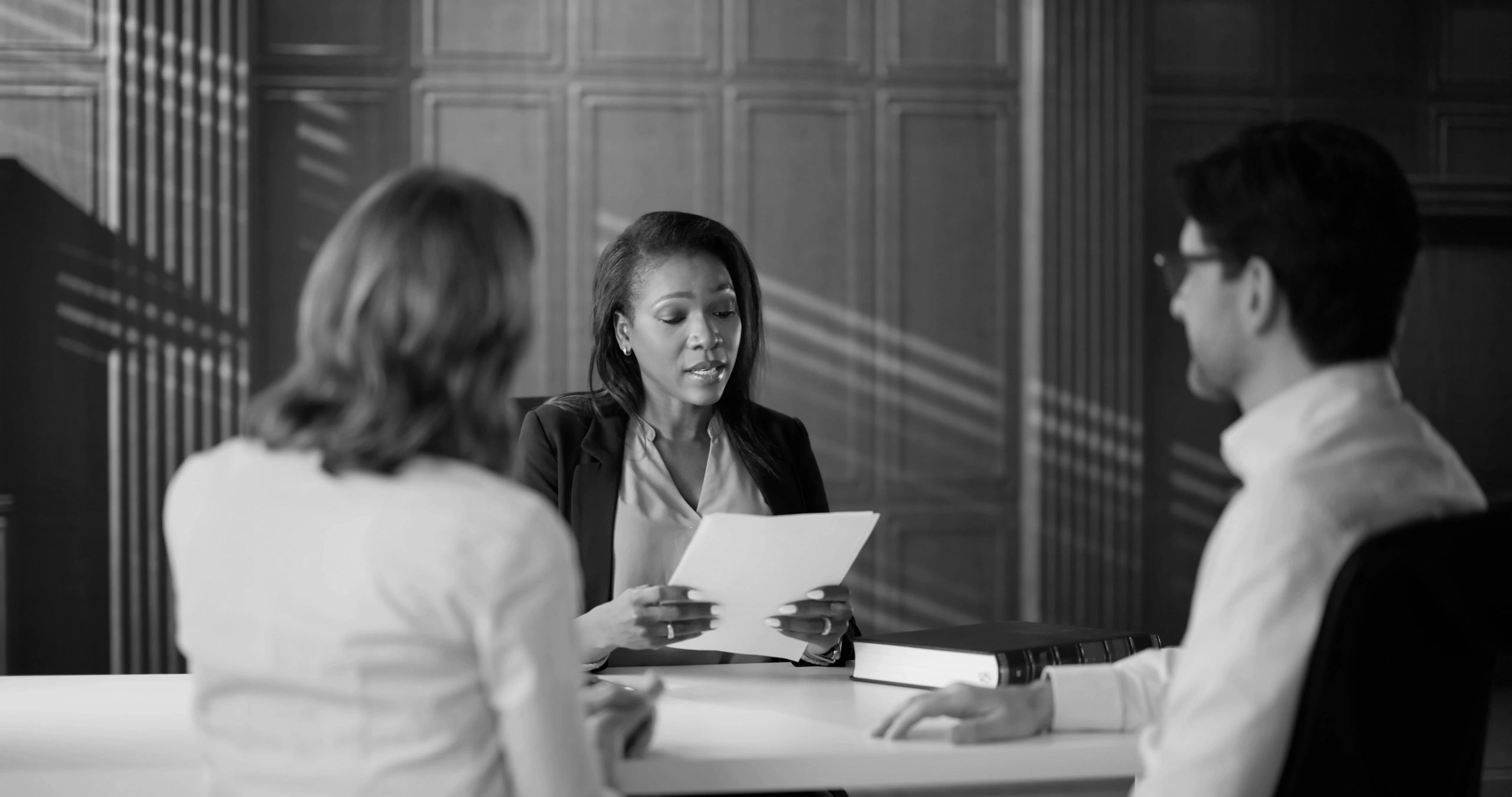A woman in a business setting reviews documents with two colleagues.