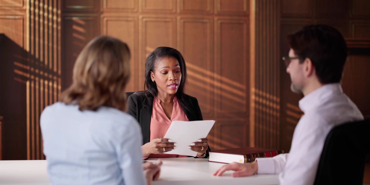 A woman reads documents to a couple in a formal office setting.