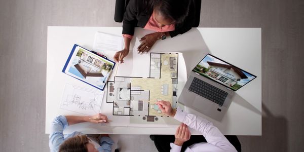 Three professionals discussing a house floor plan at a desk with a laptop and documents.