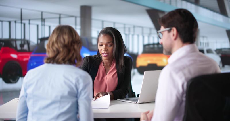 New car buyers signing contract with dealership salesperson, diverse couple.
