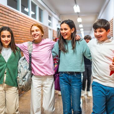 Four happy schoolchildren walking arm in arm down a hallway.