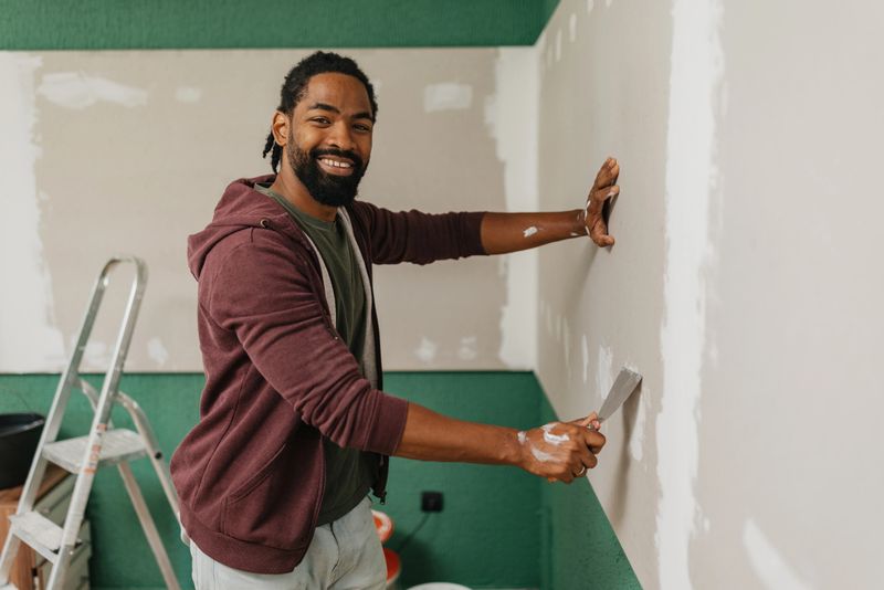 A confident man is smoothing the surface with a putty knife, showcasing commitment and skill in preparing walls for a fresh coat of paint.