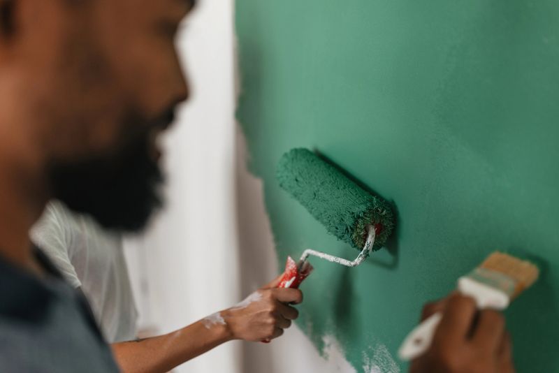 A focused couple collaborates on painting a wall, underscoring partnership and teamwork in creative home improvement tasks with a refreshing green tone.