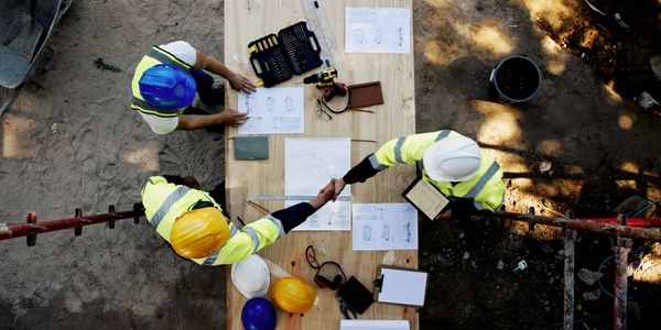 Construction workers shaking hands over project plans on a wooden table at a site.