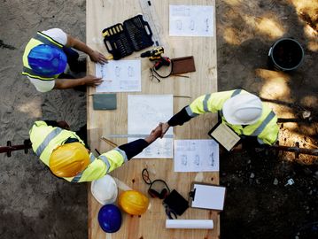 Construction workers shaking hands over building plans.