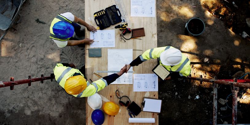 Construction workers shaking hands over project plans on a wooden table at a site.