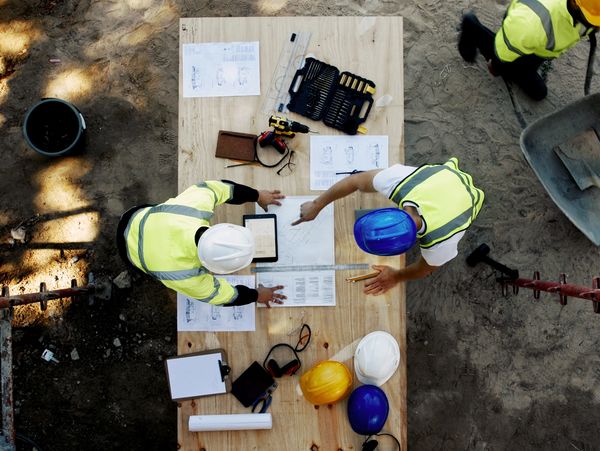Construction workers reviewing blueprints and plans on a wooden table at a site.