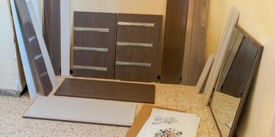 Unassembled wooden furniture parts laid out on a tiled floor.