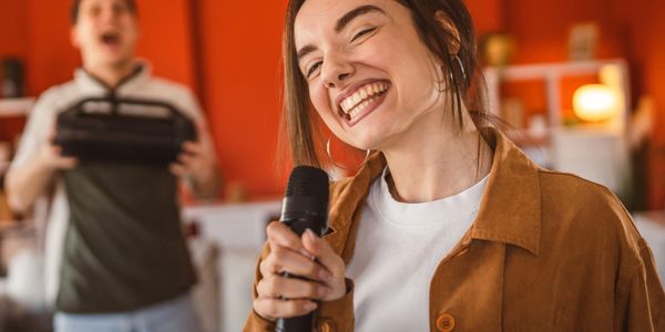 Young woman smiling and singing into a microphone indoors.