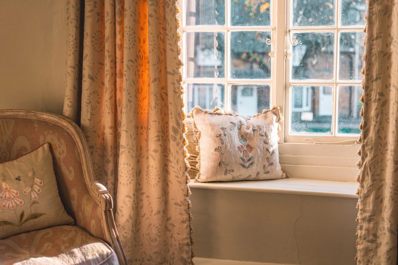 Warm sunlight illuminating cozy window sill with cushions, creating relaxing atmosphere in a charming cotswolds cottage