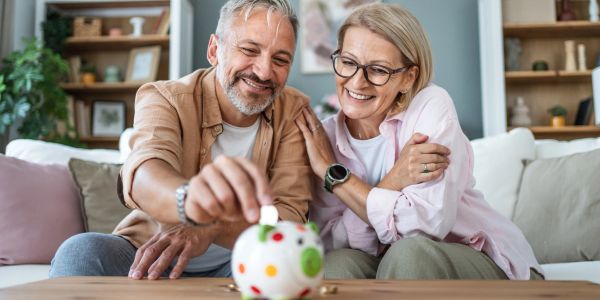 Happy elderly couple saving money in a piggy bank.