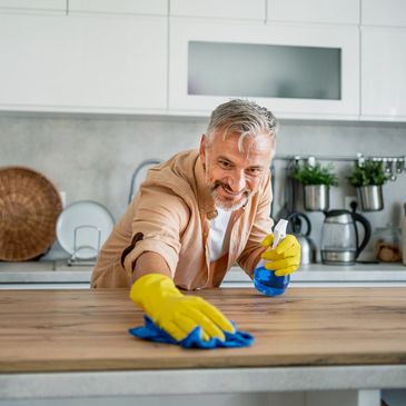 Man cleaning kitchen counter with spray and cloth, smiling.