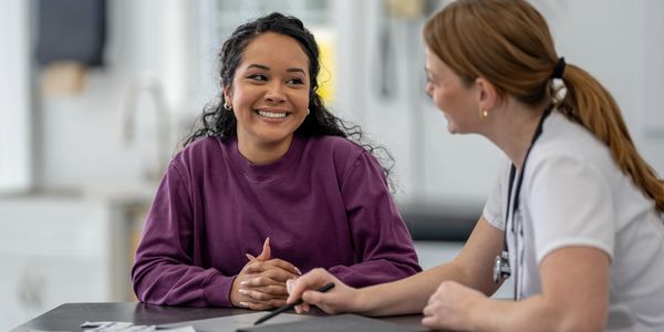 A medical professional consulting a smiling patient in a clinical setting.