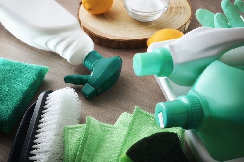 Cleaning products with natural and sustainable ingredients and tools such as disinfectant, scouring pads, cloth and gloves on a wooden table.