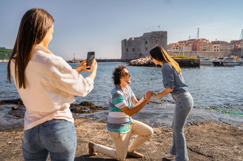 Man proposing to his girlfriend in Dubrovnik, with friend taking a photo of them