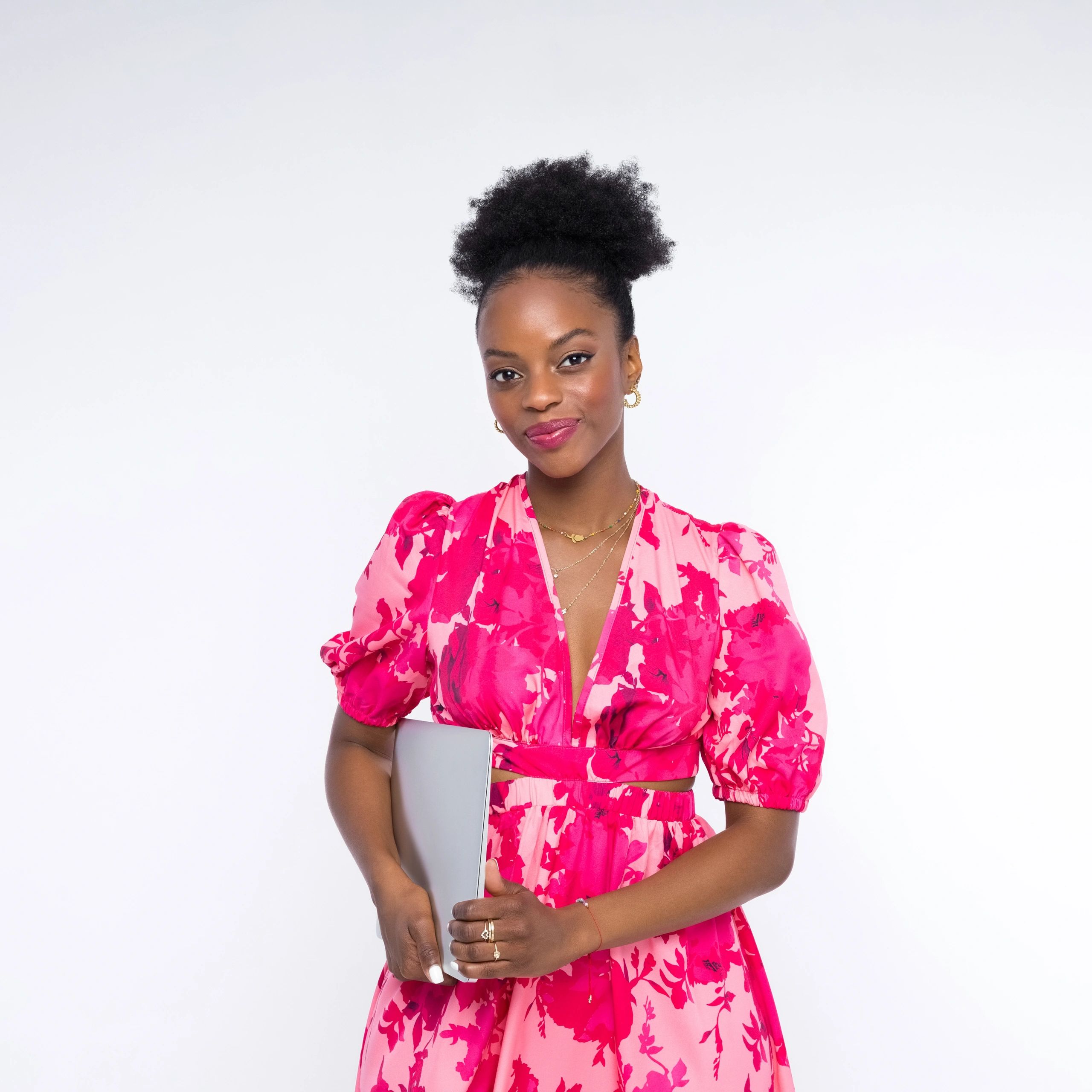 Woman in a pink floral dress holding a laptop, smiling confidently.