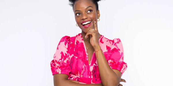 Happy woman in a vibrant pink floral dress smiling thoughtfully.