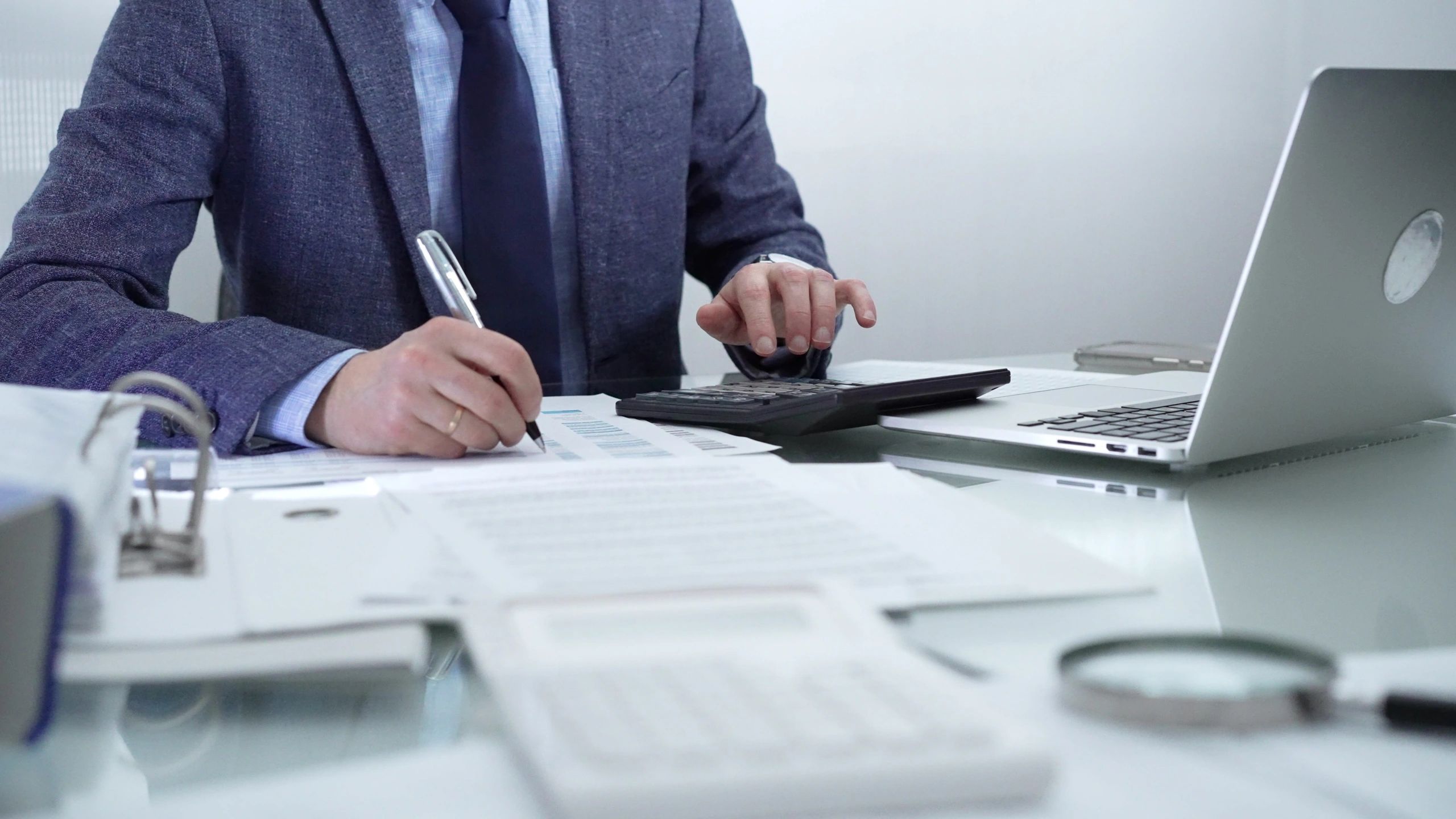 Businessman working with documents, calculator, and laptop at desk.