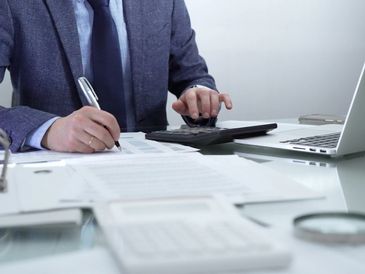 Businessperson calculating finances with documents and laptop.