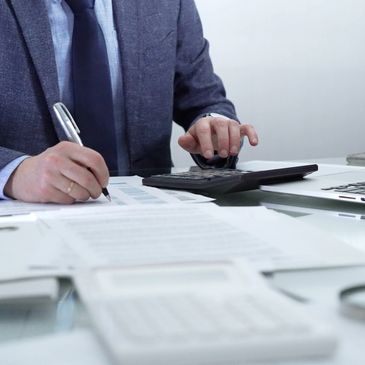 Businessman working with documents, calculator, and laptop at desk.