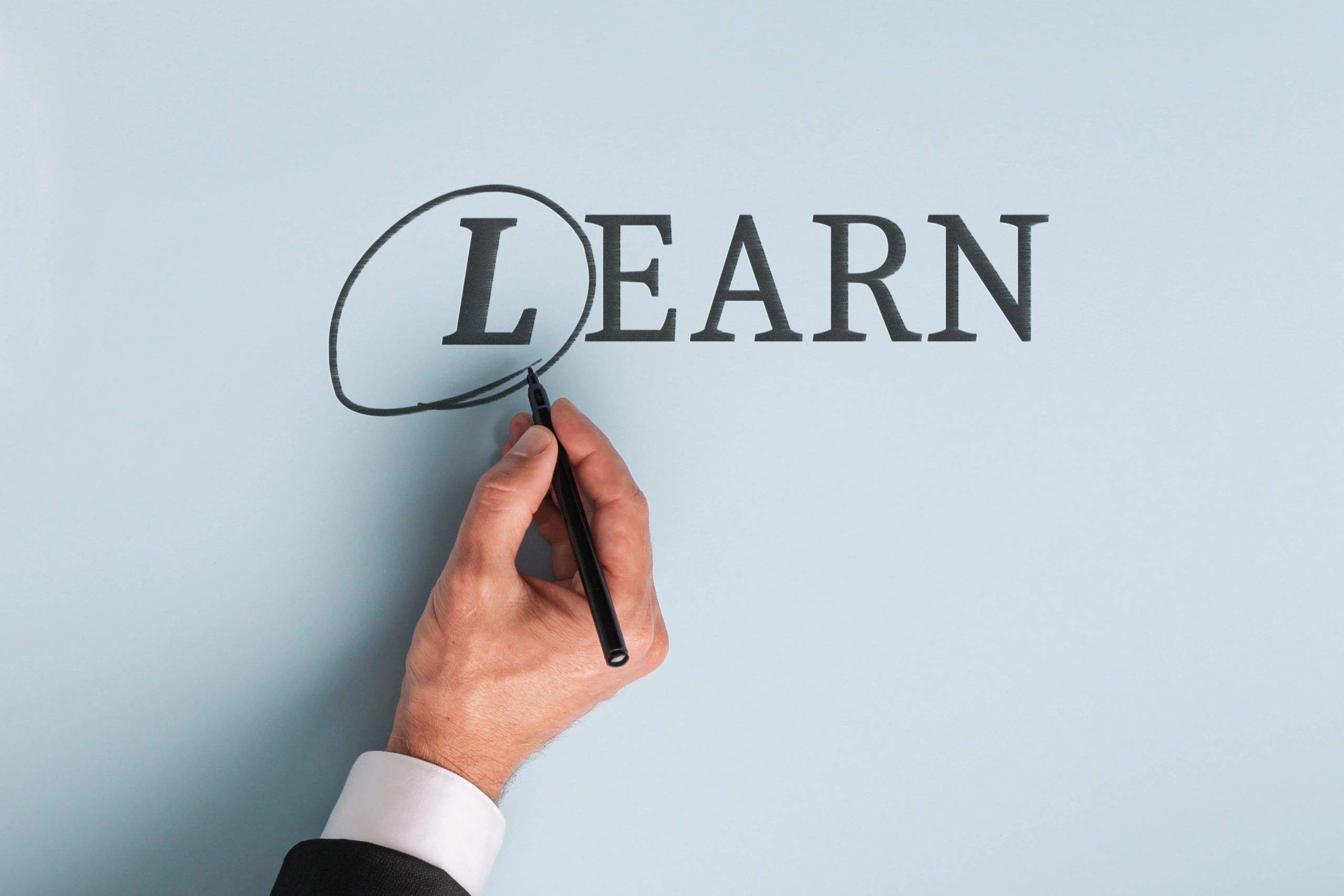 Hand circling the letter L in the word LEARN with a black marker.