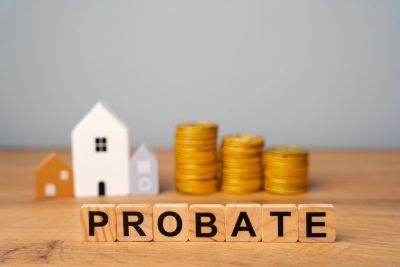Wooden blocks spell 'PROBATE' with house models and coin stacks behind.