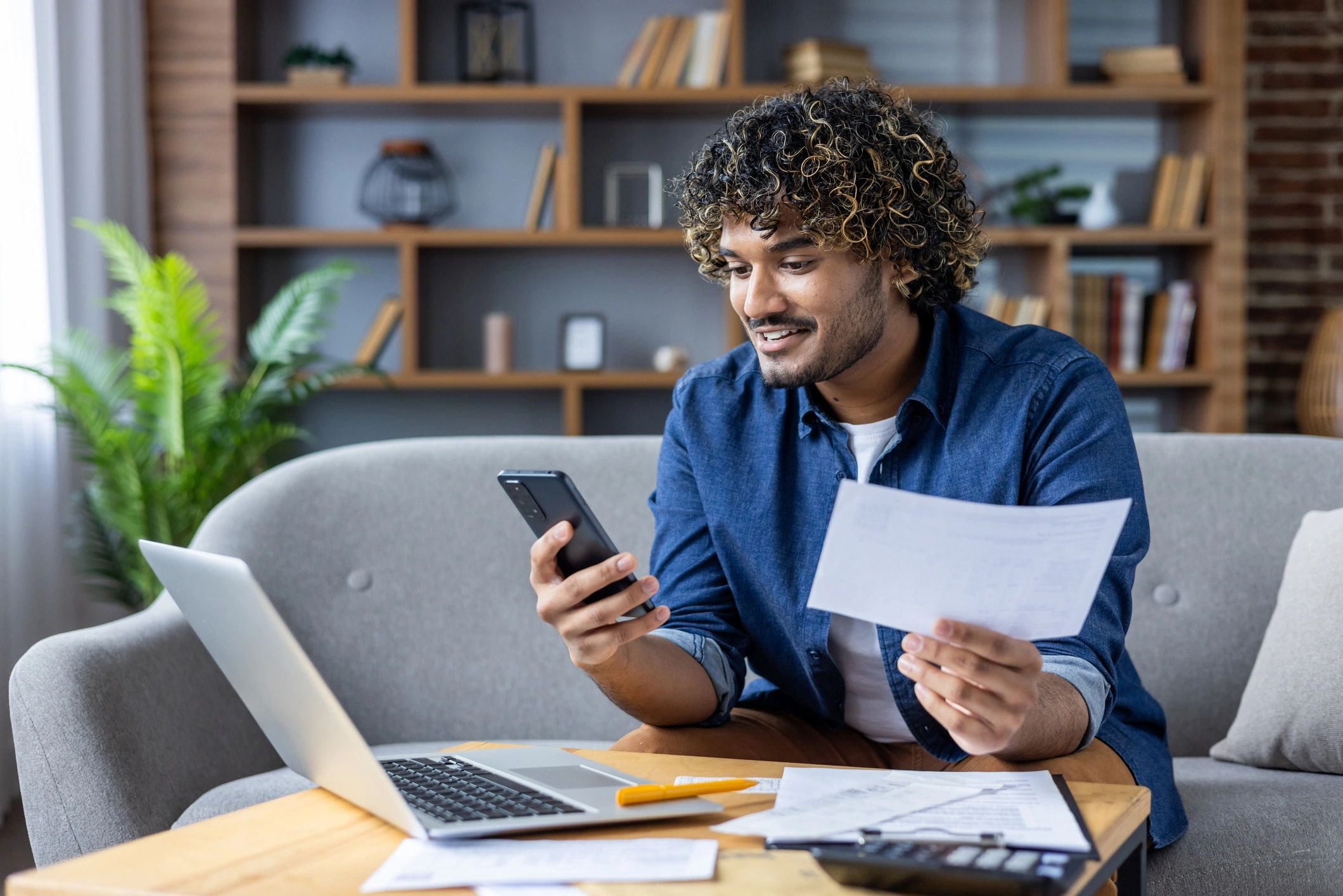 Man managing bills and finances at home with a phone and laptop.