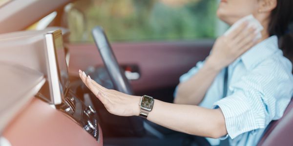 Woman cooling down inside a car using the air conditioner.