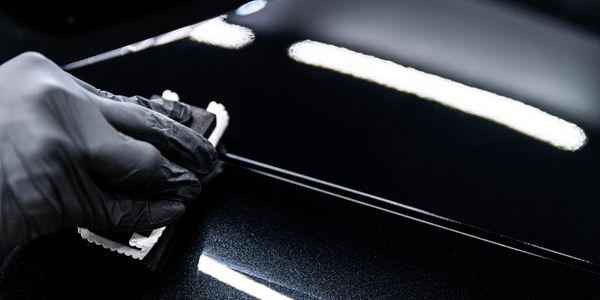 Hand in black glove polishing a shiny black surface with cloth.