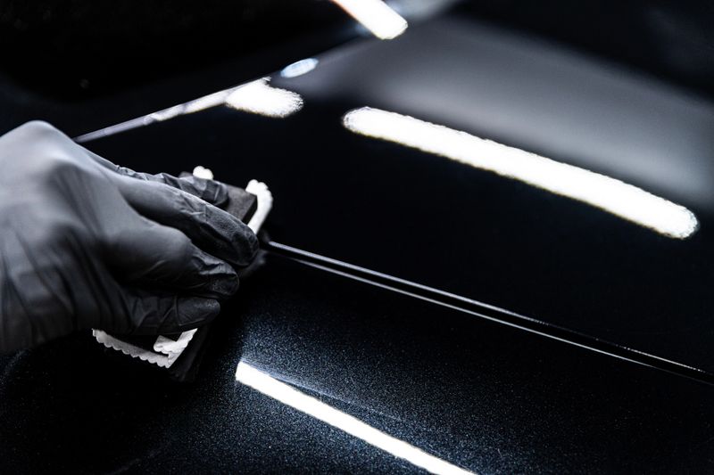 Car wash or detailing studio employee applies ceramic or graphene coating to black car paint ensuring deep gloss and advanced protection