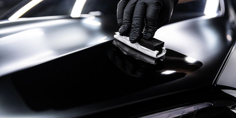 A hand with a black glove polishing a shiny black car surface.