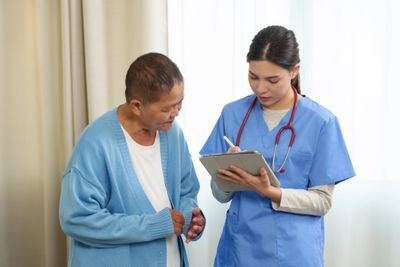 A nurse talks to a patient while taking notes on a clipboard.